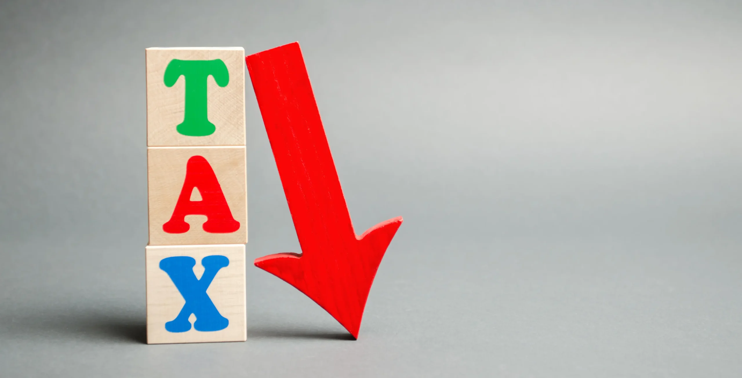 Wooden blocks with the word Tax and down arrow. Taxes reduction concept. Real estate, mortgage, goods and services taxes fall. Business and finance. Taxation